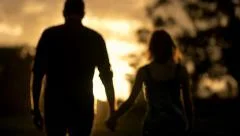 Young couple in love holding hands walking into sunset