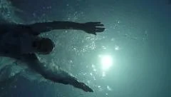 Underwater slow motion young athletic man diving into pool swimming over camera