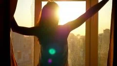 Attractive young woman opens curtains in slow motion is looking at the sunrise