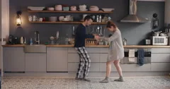 Happy young couple newly wed dancing listening to music in kitchen wearing