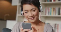 Beautiful Asian woman at home listening to music on smart phone