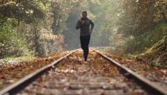 Man Jogging Up Train Tracks in Autumn Season with Leaves Falling