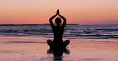 Young woman practises yoga on beach at sunset, with pink sky