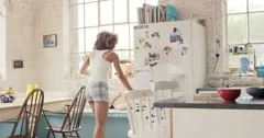 Happy curly haired  girl dancing wearing pyjamas at home in kitchen