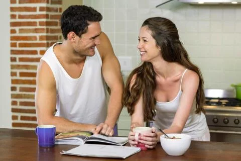 Young couple looking at each other while standing near kitchen worktop xkwx 20s, Young Adult, Man, Male, Caucasian, Woman, Female, Couple, Relationship, Lover, Home, House, Household, Homey, Apartment, Domicile, Abode, Kitchen, Worktop, Brunette, Vest, Spaghetti Top, Standing, Cup, Coffee, Looking, Each Other, Smiling, Bowl, Breakfast, Beverage, Personal Organizer, Diary, Newspaper, Information, Love, Morning, Affection, Fondness, Content, Satisfaction, Domestic Life, Closeness, Comfortable, Together, Happy, Joy, Cozy, Beautiful