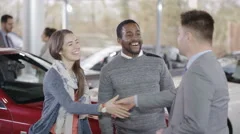 4K Happy couple in car dealers shake hands with salesman & take key to new car