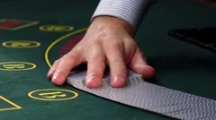 Croupier mixing cards, shows one on green table at casino