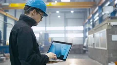 Factory worker in a hard hat is using a laptop computer with an engineering soft