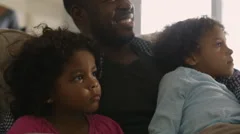 Father and daughters watching television on sofa