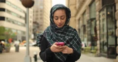 Young woman wearing hijab texting cell phone walking street