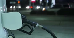 Fuel nozzle inserted in car's gas tank at gas station pump at night 4K