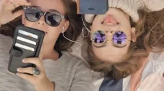 Happy teenage girls with sunglasses texting social media listening to music