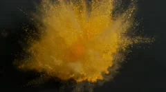 Yellow holi powder bounces off black canvas in shockwave, slow motion closeup
