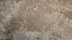 White powder particles bounce off canvas from an impact and fall in slow motion