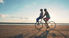 Young woman and man riding a bicycle at the shore and having some fun, slow moti