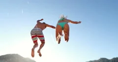 Low Angle Couple Holding Hands Jumping Into Lake In Evening