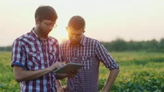 Two young farmers working in a field at sunset using tablet