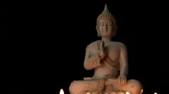 Sitting Buddha statue lit by candle light against black background