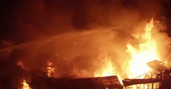 Water hose spraying on intense fire inferno in poor settlement