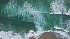 An aerial perspective looking straight down at the ocean with waves rolling in.