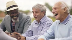 4K Happy senior male friends chatting & laughing together outdoors in the park