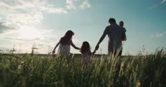 young happy Asian family goes on a green field with two children, slow motion