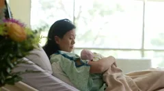 Chinese mother holding newborn baby in hospital bed