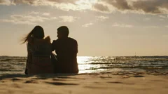 Silhouettes of couples in love, sitting on the beach, watching the sunset and a