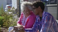 Black mother and son sitting on bench laughing at cell phone