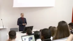Male professor speaking in front of a large audience in college