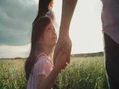 little Asian girl walking on the green field with their parents, holding the