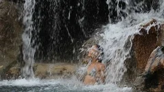 Waterfall with woman in bikini bathing and swimming in natural pool on travel