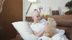 Cancer patient woman lying on the sofa and playing with a little cute dog