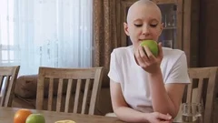 Cancer patient woman sits at the table eats an apple and looks at the camera
