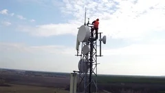 worker servicing cellular antenna in front of sunlight, drone view of