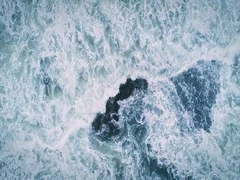 Aerial flying over waves crashing on rocks coastline ocean surf in california