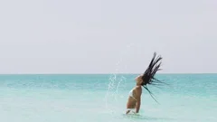 Sexy beautiful girl with long hair in bikini making a splash of water on beach