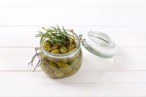Jar of pickled caper berries on white wooden background
