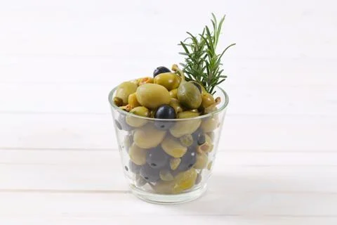 Glass of pickled olives, capers and caper berries on white wooden ...