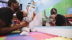 Black father playing on floor with baby son