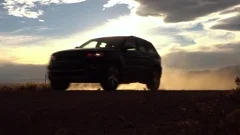 SLOW MOTION CLOSE UP Black SUV car driving on dusty dirt road at golden sunrise