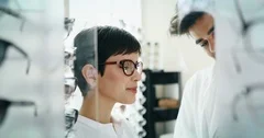 Beautiful woman with optician trying eyeglasses at optics store