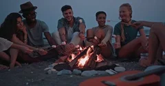 Young multi-ethnic hipster friends roasting marshmallows over bonfire at beach