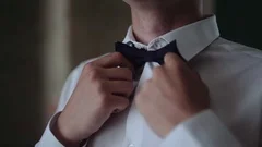 Man straightens bow-tie. Young man puts and adjusts classic black bow tie