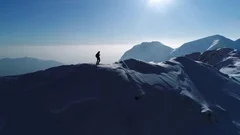Aerial, slow motion - Man hiking on top of snowy mountain at beautiful sunset