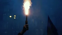 Protester holding burning flare. Night street in smoke. Hand close-up