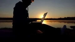 Middle aged writer types a fairy tale on a computer at sunset