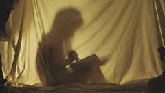 Silhouette of little girl reading a book inside a blanket fort in the evening, l