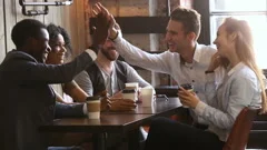 Multi-ethnic young friends laughing giving high-five at meeting in coffeehouse
