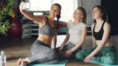 Attractive young women are taking selfie after yoga class in light modern gym in
